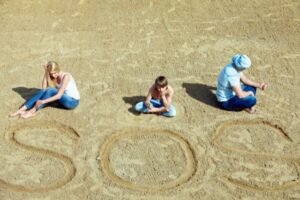 Familia sentada sobre la arena con el mensaje "SOS" escrito, representando una crisis familiar